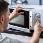 Young Man Preparing Food In Microwave Oven On Kitchen Counter